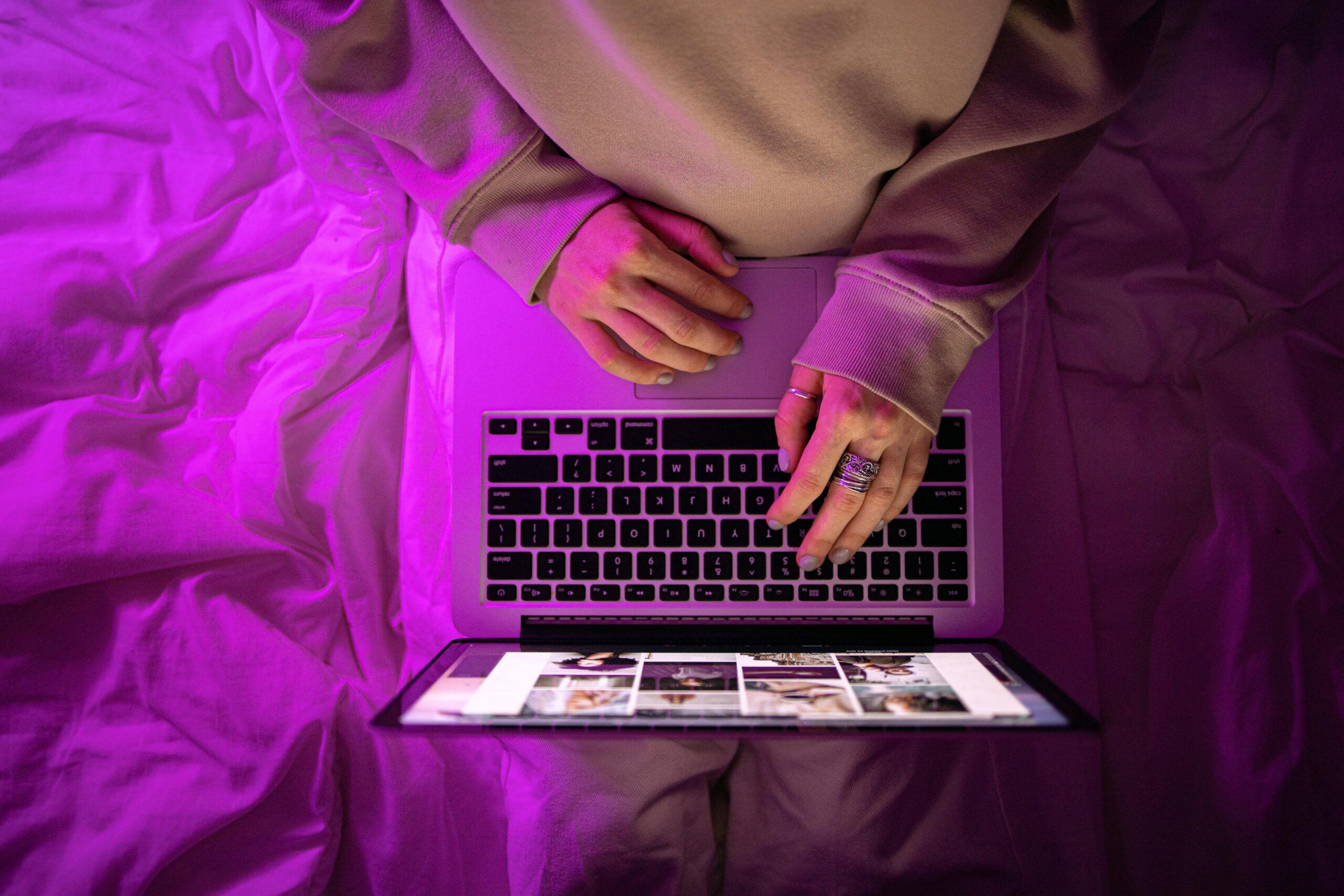 Top view of unrecognizable person using laptop with neon purple lighting, creating a vibrant high-tech atmosphere.