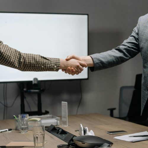 Two business professionals shaking hands in a modern meeting room, symbolizing successful collaboration.
